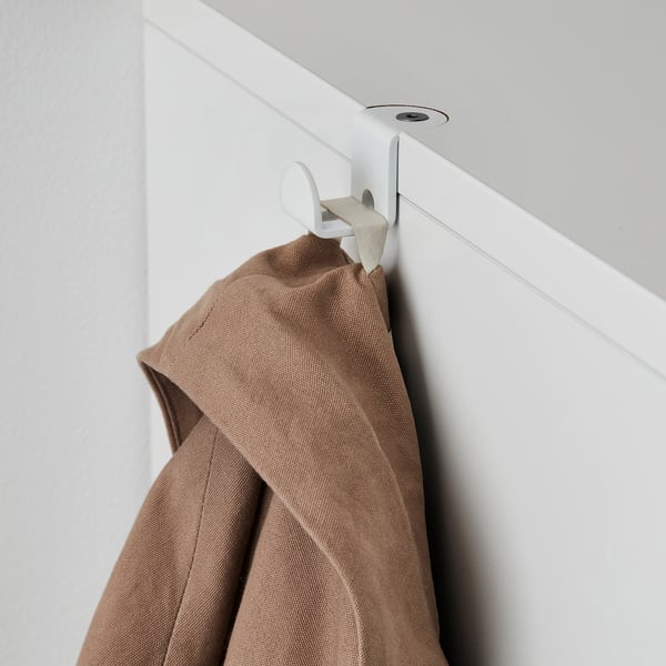 Une veste beige est suspendue à un crochet blanc fixé à un rail mural, mettant en valeur la flexibilité de rangement GALANT.