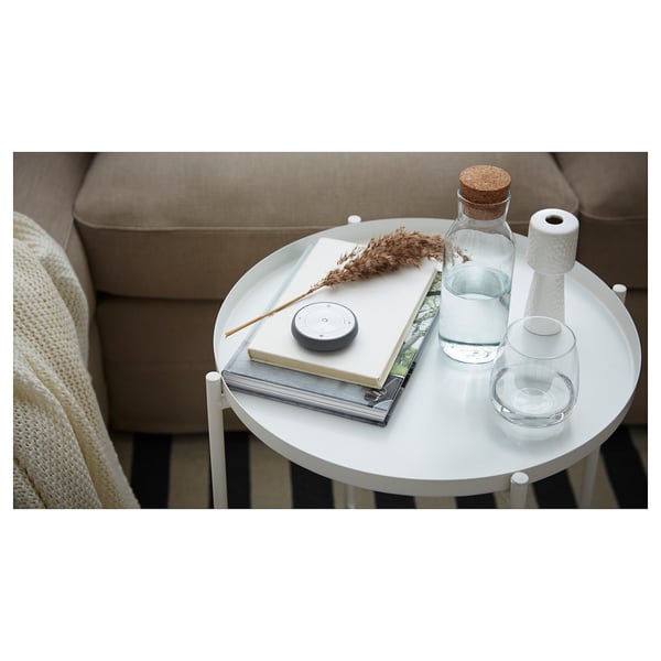 Table d’appoint ronde minimaliste avec canapé beige, plateau blanc, livres, bouteille d’eau et haut-parleur. Design moderne et fonctionnel.