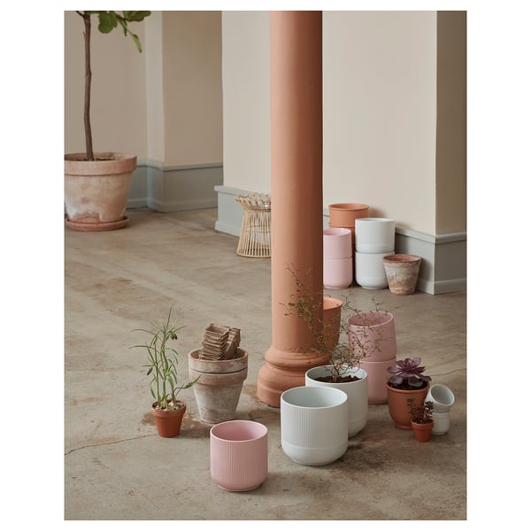 Plusieurs jardinières en poterie de différentes nuances et tailles, exposant des plantes. Des pots empilés et des motifs variés, disposés à l’intérieur sur un sol en béton.