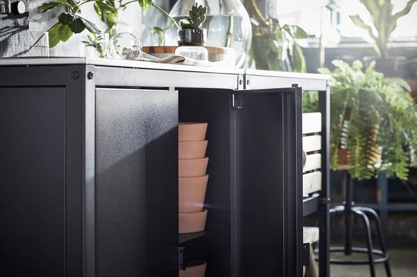 Armoire de cuisine extérieure noire avec des pots en terre cuite empilés, décorés de plantes.