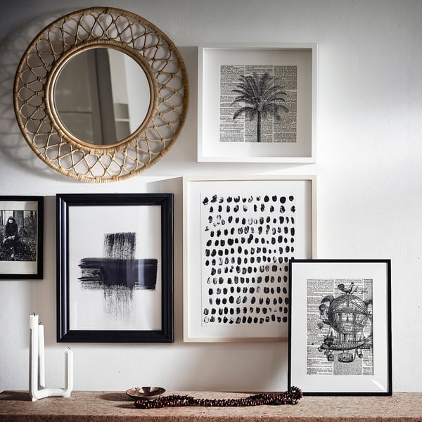Présentoir mural Miroir en rotin GRINSBOL entouré d’œuvres d’art encadrées en noir et blanc, créant une composition vibrante et texturée.