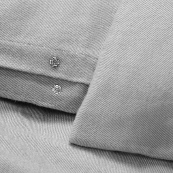 Gros plan d’une literie en flanelle de coton gris douce et texturée avec fermetures à pression en métal, mettant en valeur un tissu de haute qualité et un savoir-faire détaillé.