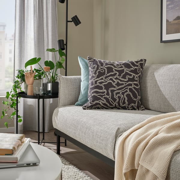 Salon confortable avec coussin GULDFLY, canapé gris, oreillers décoratifs, couverture, plantes, ordinateur portable, livres, photo encadrée, lampe.