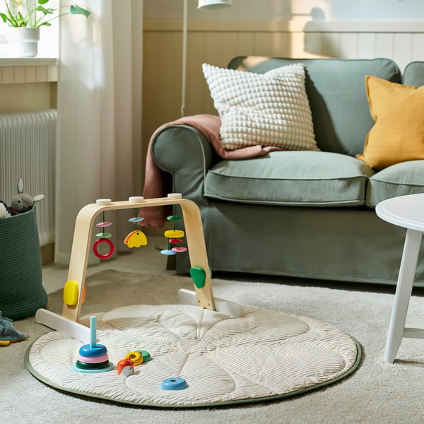 Salon confortable avec canapé bleu clair, arche d’activité de bébé colorée et couverture blanche ronde et matelassée sur le sol.