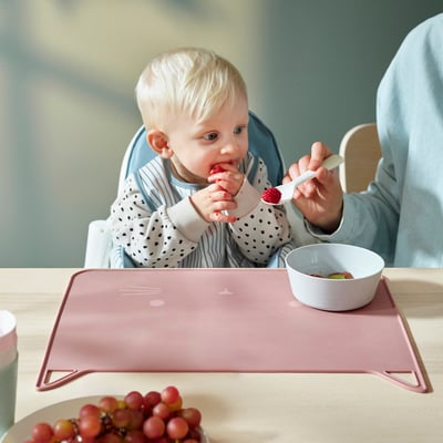 Bébé mangeant des fruits dans une chaise haute avec des raisins à proximité.