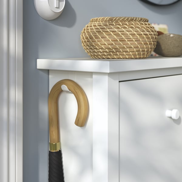 Le parapluie à poignée en bambou s’appuie sur une armoire en bois blanc avec un panier tressé et un bocal en verre sur le dessus.