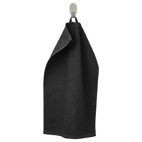 La serviette noire GULVIAL s’accroche soigneusement à un crochet argenté, mettant en valeur son tissu en coton doux et texturé.