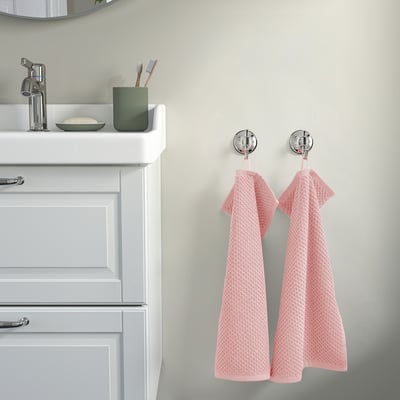 Une salle de bain avec un lavabo blanc, une armoire et des serviettes GULVIAL roses sur des crochets chromés. Coton doux et moelleux.