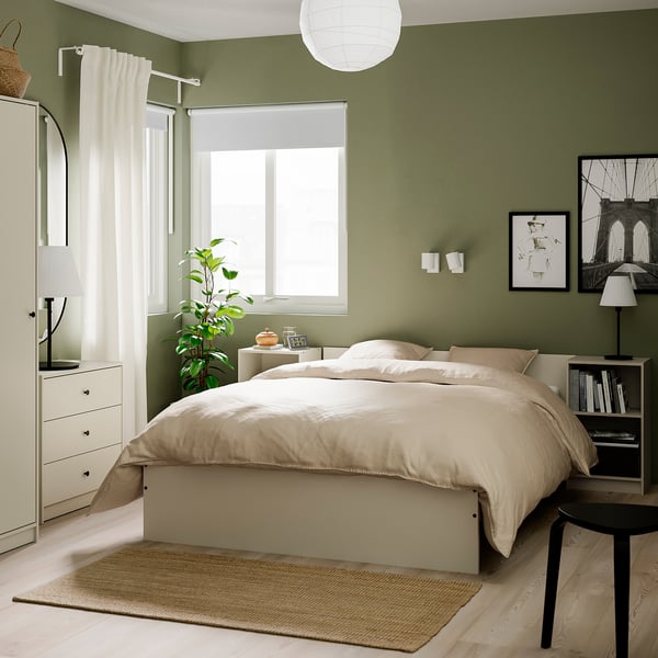 Coffre GURSKEN blanc moderne dans la chambre à coucher, idéal pour les petits espaces. Grand, à côté de la fenêtre avec lampe et plante.