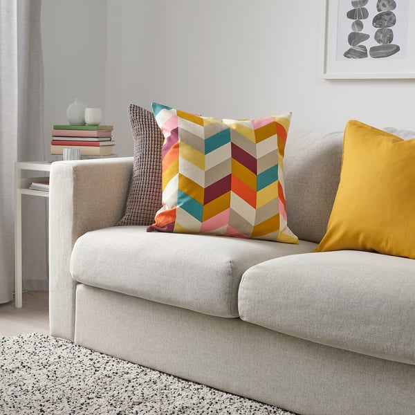 Coussin chevron et oreiller jaune sur canapé gris, livres et vase sur table blanche.