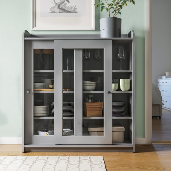 Vitrine HAUGA grise avec portes vitrées et étagères ouvertes, permettant de ranger des plats, des bols et des verres dans un salon.