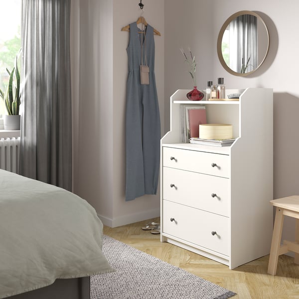 Chambre confortable avec coffre HAUGA blanc, parquet en bois clair, rideaux gris et plantes.