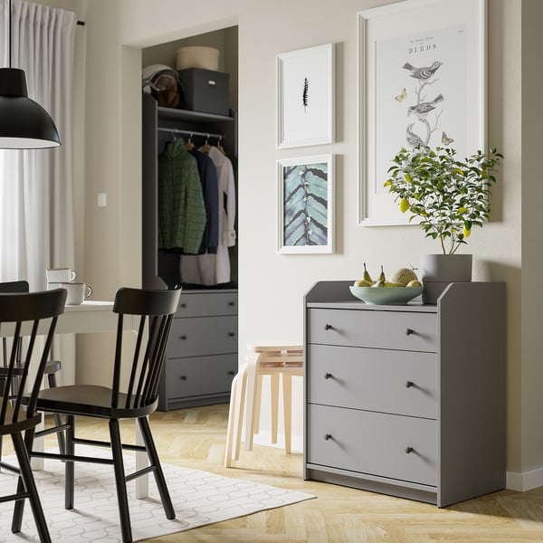Salon moderne avec coffre HAUGA gris, chaises noires, suspension, tapis blanc, art mural.