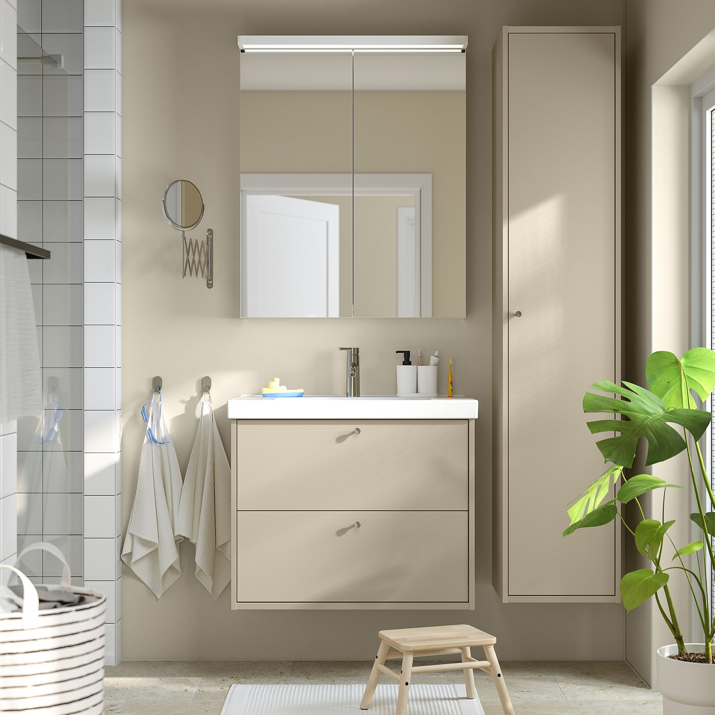 Salle de bain élégante avec meuble-lavabo beige HAVBÄCK, miroir, plante verte, serviettes et panier à linge.