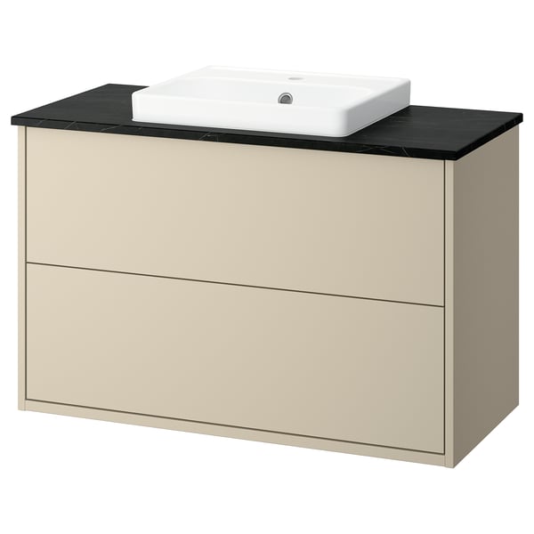 Un meuble de salle de bain beige HAVBÄCK avec un plan de travail noir et un lavabo carré blanc. Il possède deux tiroirs pour le rangement.