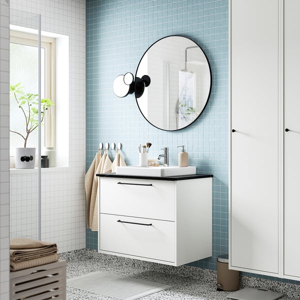 Meuble moderne blanc avec miroir rond, fixé au mur, carreaux bleu clair, deux tiroirs, minimaliste.