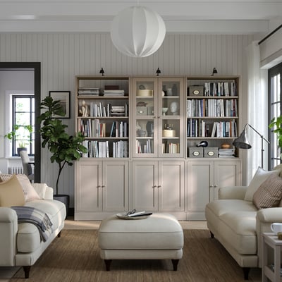 Salon moderne avec des bibliothèques en pin gris clair HAVSTA remplies de livres, un canapé et un pouf blancs, des murs gris et des lampes suspendues.