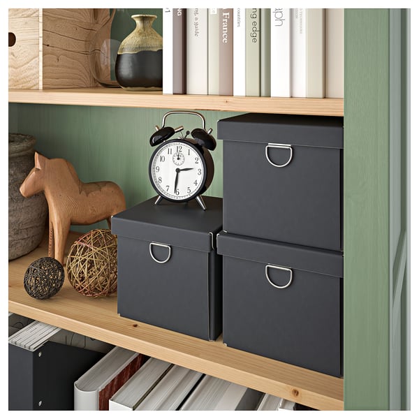 Une bibliothèque HEMNES dans une teinte vert-gris apaisante avec des étagères en bois teinté. Il expose des objets de décoration, des livres et des boîtes de rangement sur les étagères.