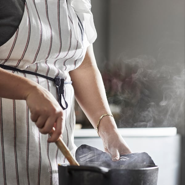 Personne portant un tablier rayé blanc cuit sur la cuisinière.