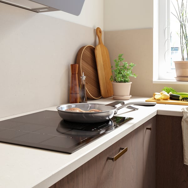 Cuisine moderne avec plaque de cuisson à induction, poêle à frire, ustensiles en bois et produits frais.
