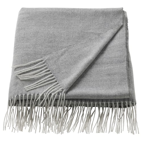 Un plaid gris plié HOLMVI avec des bords frangés, fabriqué à partir de polyester recyclé.