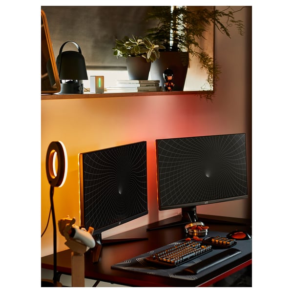 Une configuration de bureau de jeu noir avec deux moniteurs, un clavier ergonomique, une lampe annulaire et des décorations végétales.