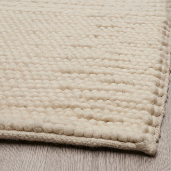 Tapis texturé tissé beige sur un plancher en bois. Des motifs complexes et un savoir-faire de haute qualité.