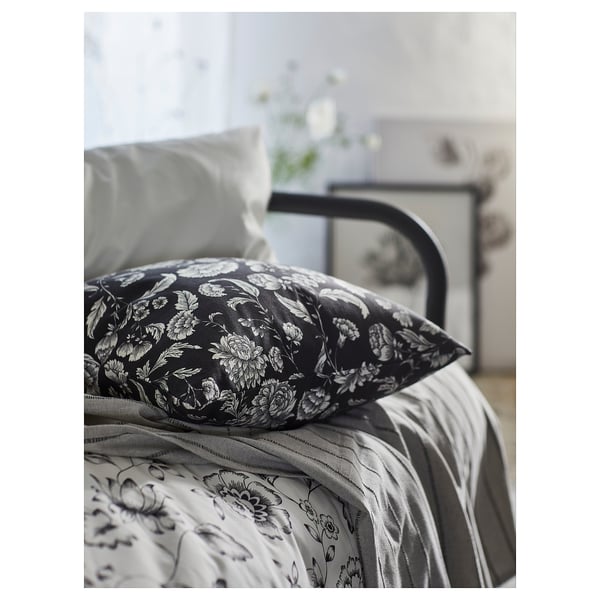 Oreiller de lit noir avec motif floral blanc sur literie à motifs. Cadre de lit en métal apparent.