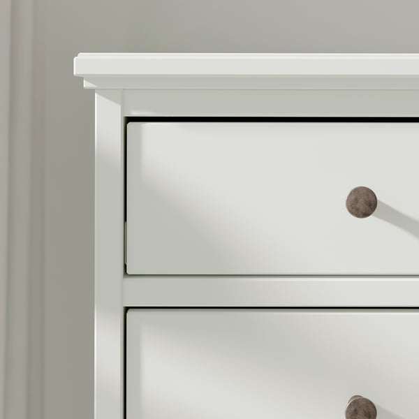 Commode en bois blanc avec boutons ronds, avec trois tiroirs, et design simple.
