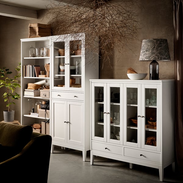 Salon moderne avec armoire blanche IDANÄS, exposant la verrerie et la décoration. Canapé vert, branches décoratives et lampe.