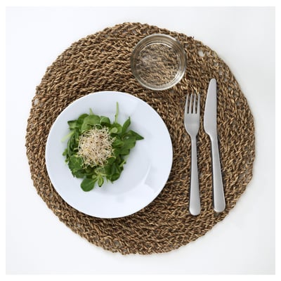 Une assiette blanche avec de la salade verte, du verre et des ustensiles sur un set de table tissé.