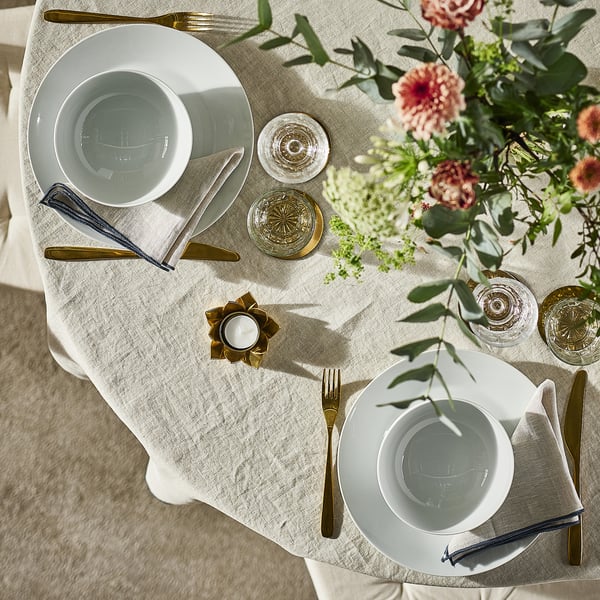 Set de table avec des assiettes IKEA 365+ blanches, des couverts en or, des verres et un centre de table floral.