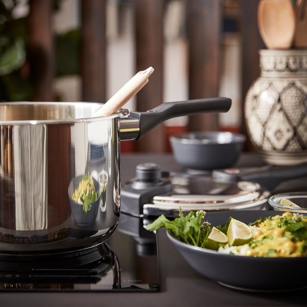 Un autocuiseur en acier inoxydable brillant se trouve sur une cuisinière. A proximité, un bol de salade composée et des quartiers de citron vert. Un vase complexe décore le comptoir.
