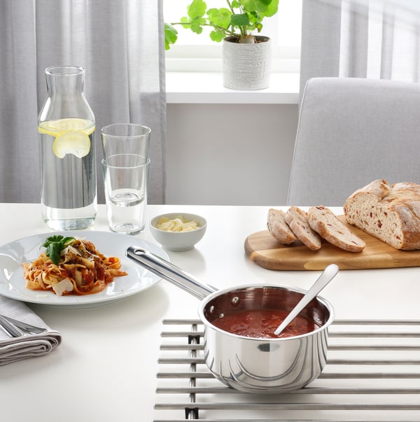 Une configuration de cuisine avec une casserole de sauce, des tranches de pain et une carafe sur une table.