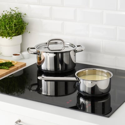 Ensemble de casseroles en acier inoxydable sur une plaque de cuisson à induction noire, dont une contenant du liquide, présentant des poignées résistantes à la chaleur et une répartition uniforme de la chaleur.