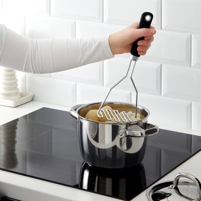 La personne utilise un presse-purée IKEA sur une cuisinière. La poignée du presse-purée a une prise ferme et une encoche pour éviter de glisser.