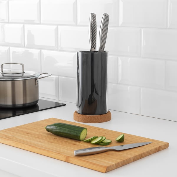 Bloc de couteaux ikea noir avec des couteaux à côté d’une planche à découper en bambou et de concombre tranché.