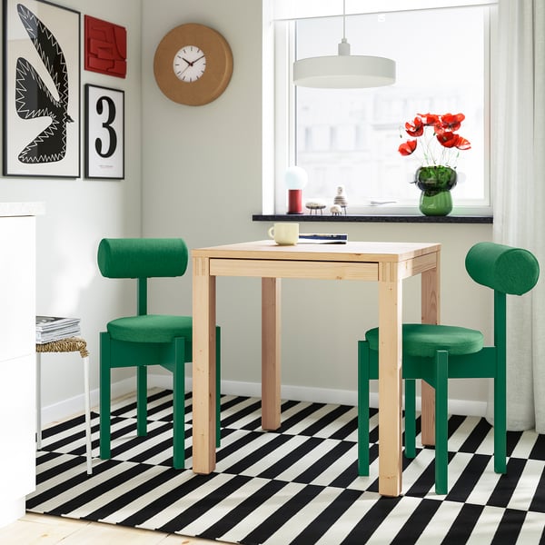 Cuisine moderne IKEA : table en bois clair, chaises rembourrées, sols audacieux, peinture murale, horloge, fleurs