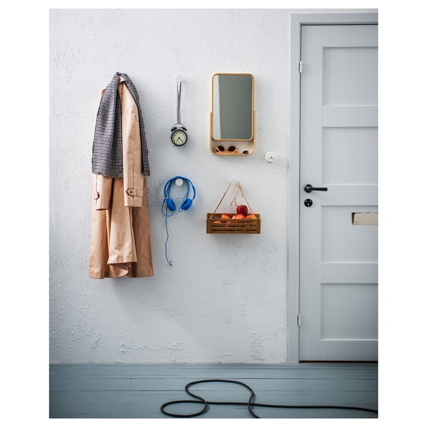 Entrée bien rangée avec manteau, écouteurs, horloge, miroir, pommes près de la porte.