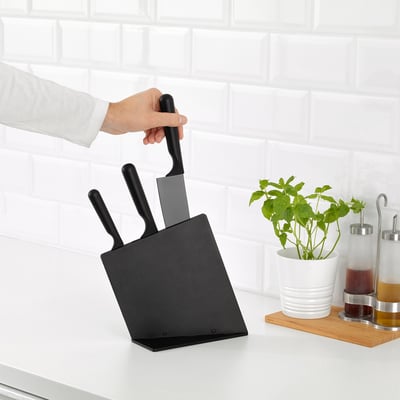 Personne saisissant un couteau dans un bloc noir sur le comptoir de la cuisine, à côté de plantes et de condiments.