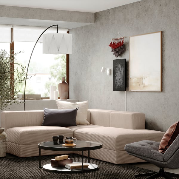 Salon moderne avec canapé sectionnel beige, table basse, chaise grise, grande fenêtre et œuvres d’art abstraites.