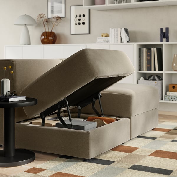 Canapé beige moderne avec un espace de rangement révélant un siège relevable. Des livres et des couvertures rangés en dessous.