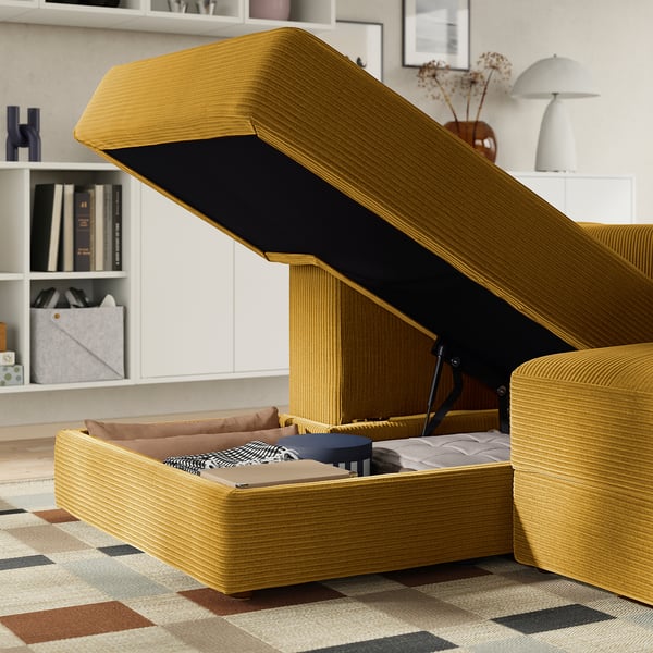 Canapé jaune moutarde avec rangement ouvert, coussins révélateurs et couverture pliée à l’intérieur ; Sur fond de pièce moderne.