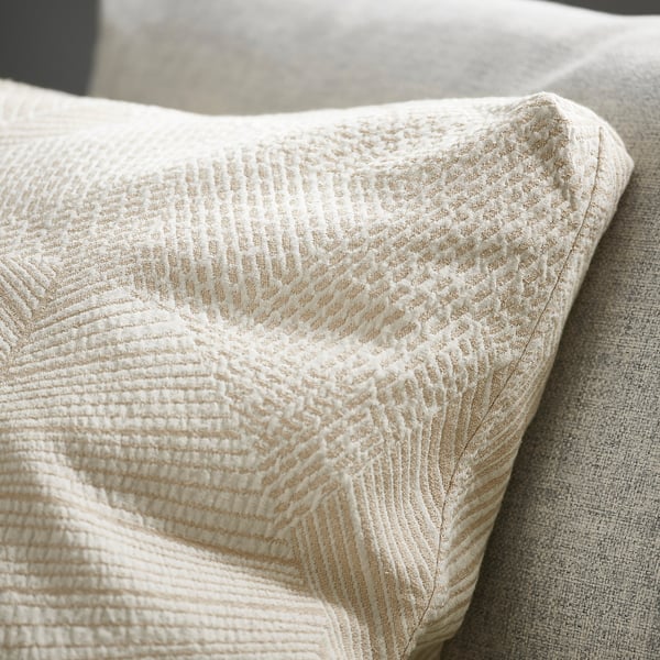 Housse de coussin blanc cassé avec motif texturé et feuillu ; Coins finement détaillés, caissonnés.