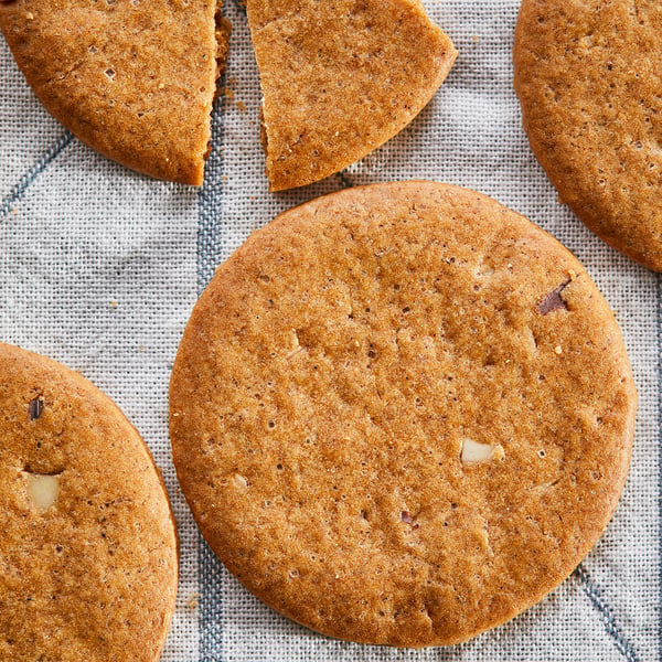 Six biscuits au gingembre KAFFEREP dorés, ronds, croustillants et parsemés de minuscules miettes d’amandes, posés sur un chiffon gris clair.
