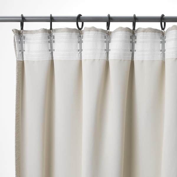 Trois rideaux beiges avec des dessus plissés sont suspendus à une tringle métallique, avec des crochets pour des ajustements faciles et de l’intimité.