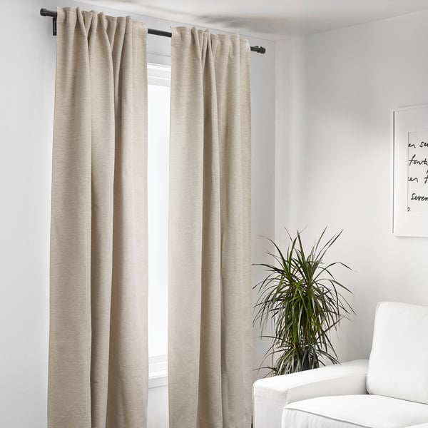 Les rideaux KALAMONDIN, beiges, fabriqués à 100 % en polyester recyclé, sont longs, élégants et minimalistes, couvrant la fenêtre à côté des meubles blancs.