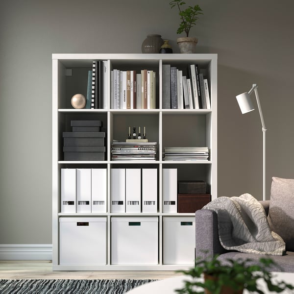 Étagère KALLAX blanche avec livres, classeurs et décoration. Comprend une plante en pot et un lampadaire.