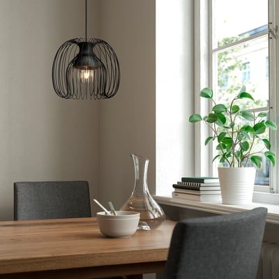 Configuration de salle à manger moderne avec table en bois, chaises sombres, lampe KALLFRONT, bol, carafe, livres et plante.