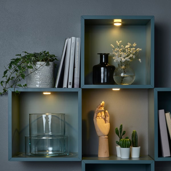 Étagère avec plantes, livres, vases et spots led intégrés. Chaque compartiment est éclairé, mettant en valeur la décoration et les matériaux de lecture.